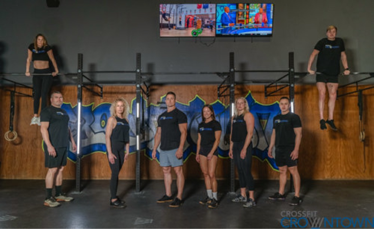 CrossFit CrownTown coaching team together in front of the gym mural