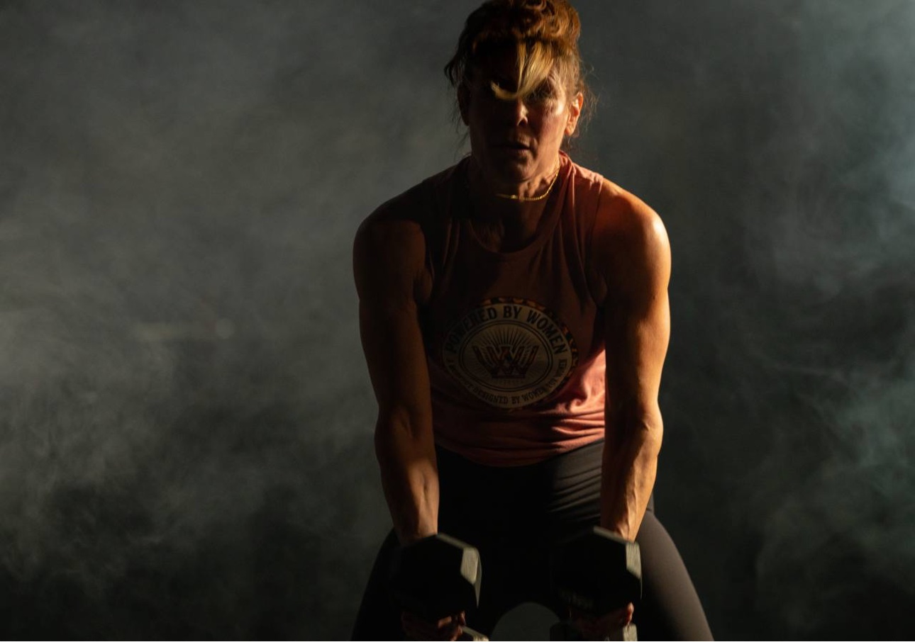 Athlete in a Powered By Women tank training with dumbbells